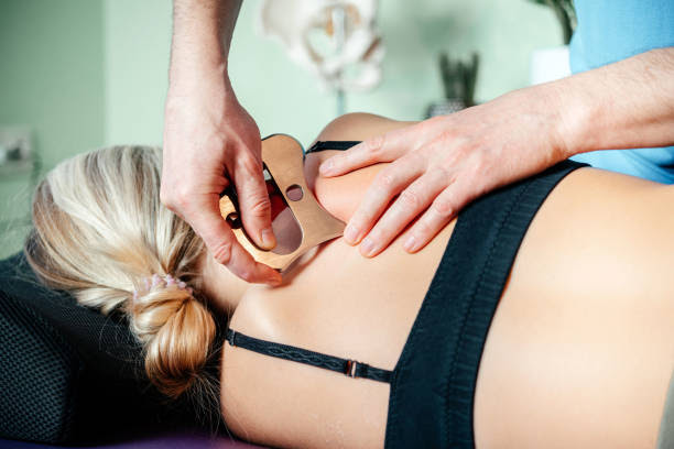 Close-up of a practitioner using a stainless steel Graston tool on a woman’s upper back to relieve muscle tension and promote healing
